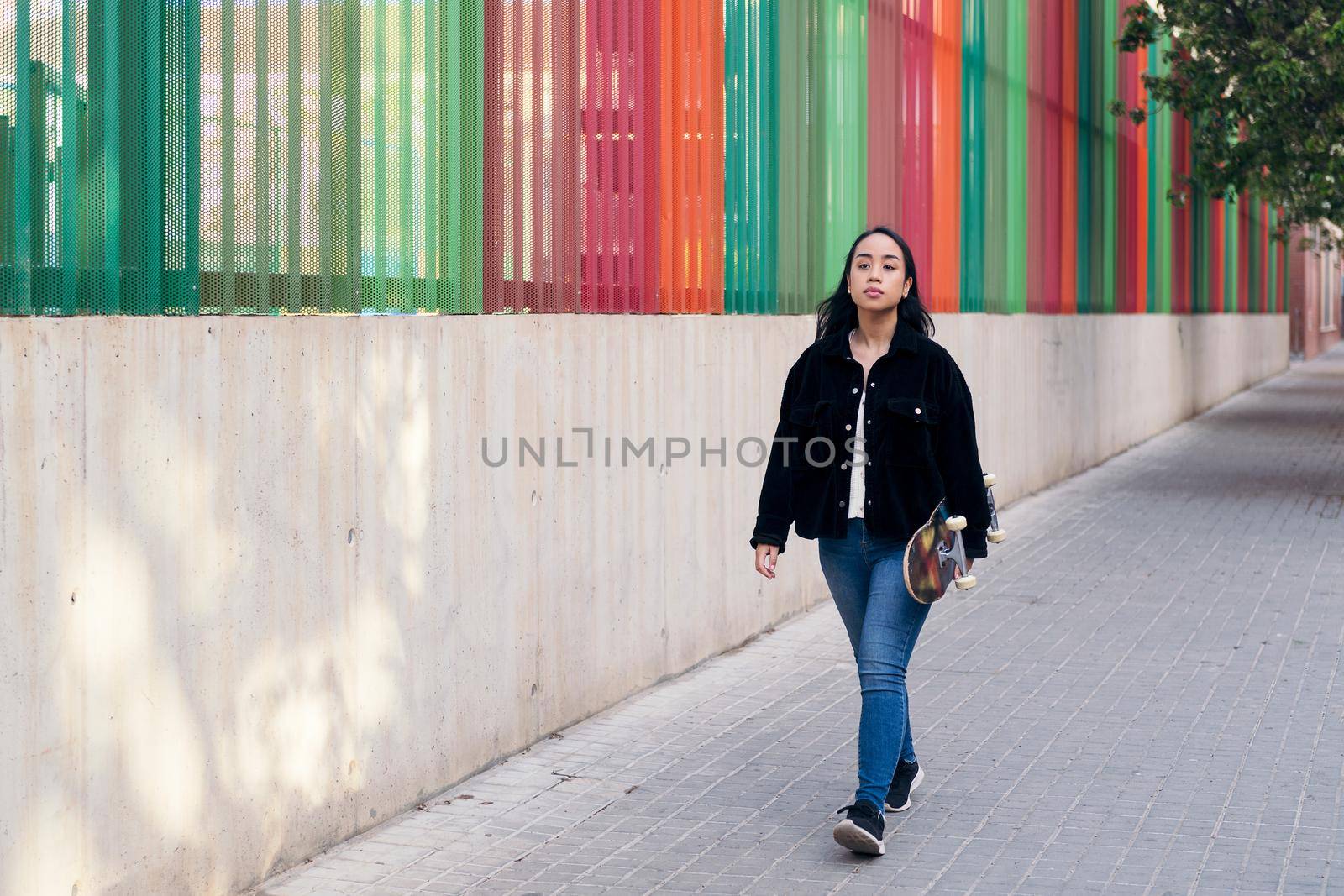 asian teenage girl walking down the street with her skateboard in her hand
