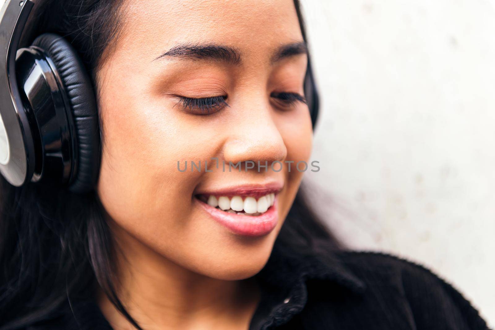 portrait of a cheerful young asian woman with headphones enjoying listening to music outdoors