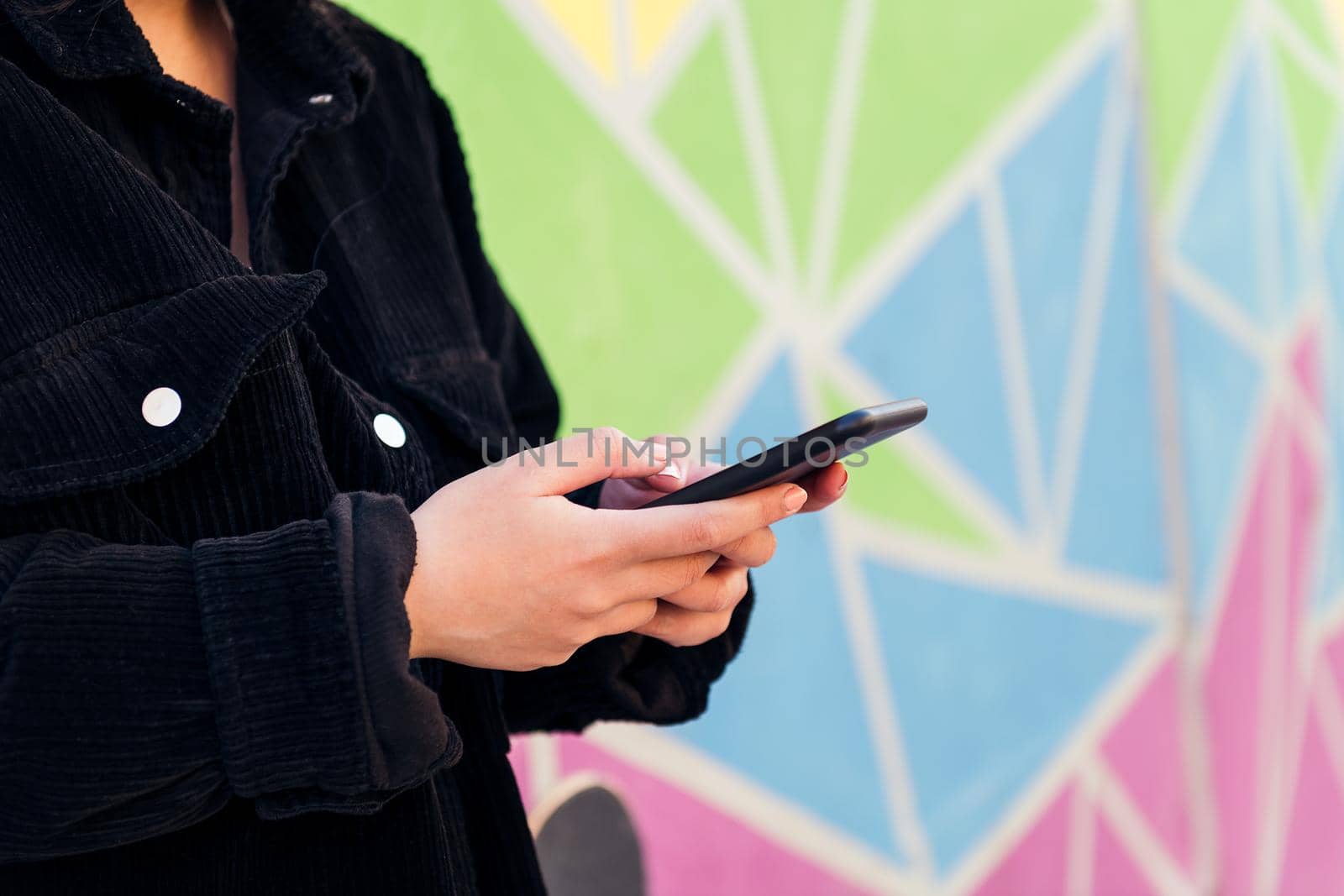 close up of the hands of an unrecognizable young woman typing on her cell phone against a colorful wall