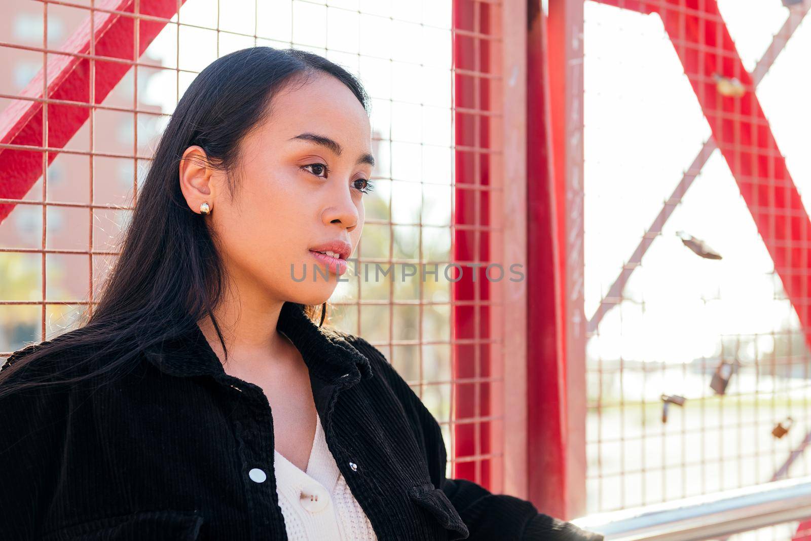 portrait of a young asian woman outdoors leaning against a red fence
