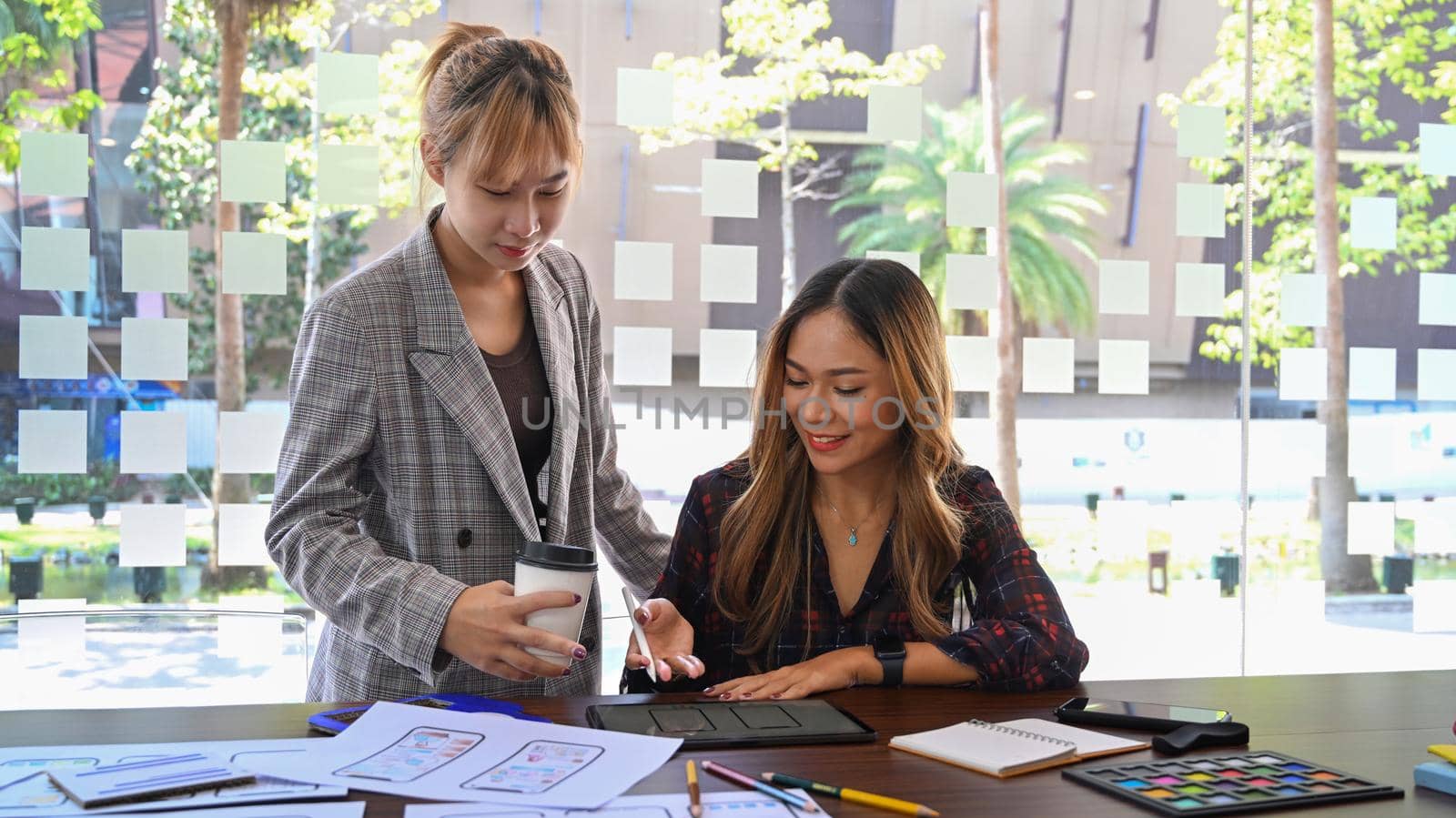 Two young creative women are brainstorming and working on mobile app interface wireframe design together.