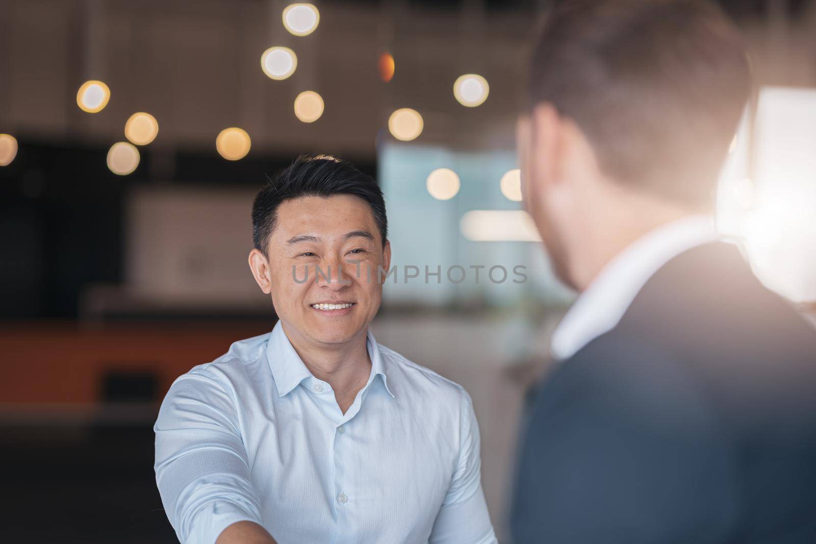 Close up of two smiling businessmen are handshaking after a successful deal in modern office by Yaroslav_astakhov