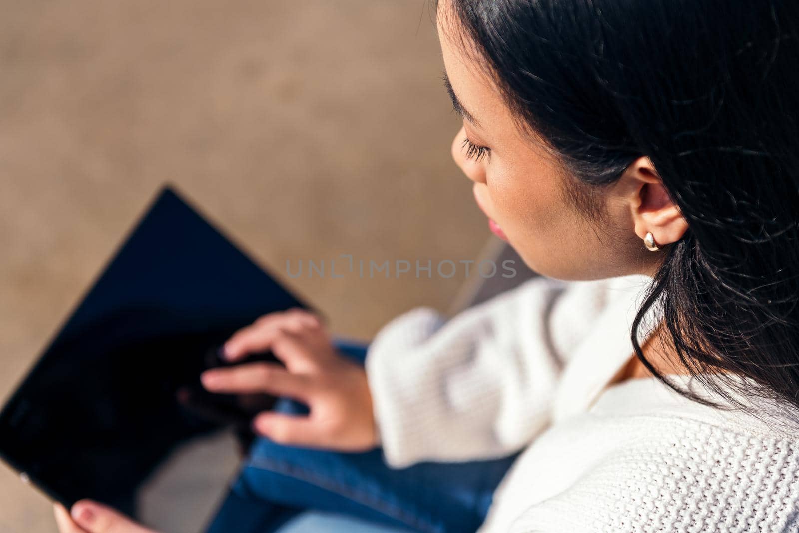 unrecognizable young woman sitting on the street using her tablet
