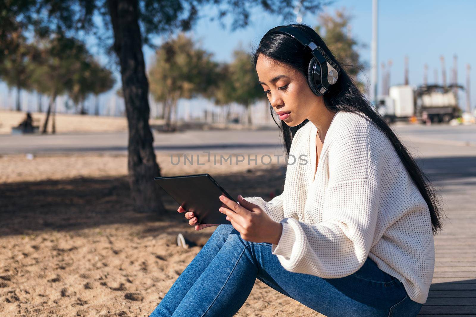 asian young woman with headphones watching videos on her tablet sitting outdoors