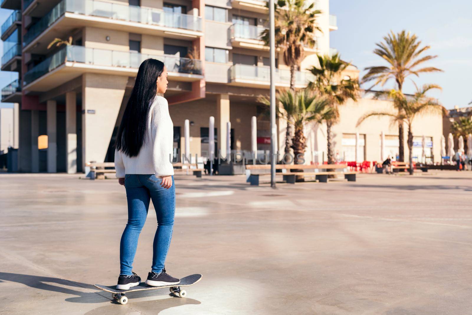 rear view of a young asian woman riding a skateboard in the city