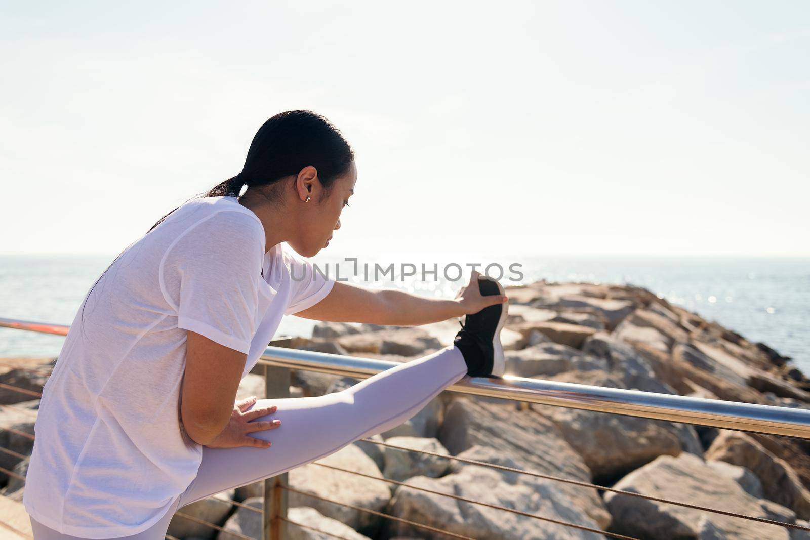 young asian sportswoman stretching legs by the sea, concept of sport and active lifestyle