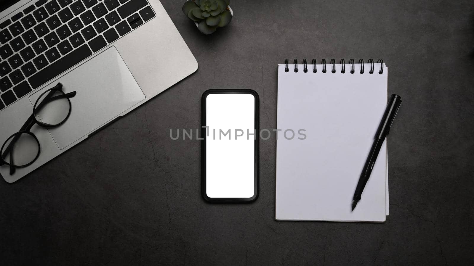 Black office desk with smart phone, laptop computer and notepad. Top view, flat lay.