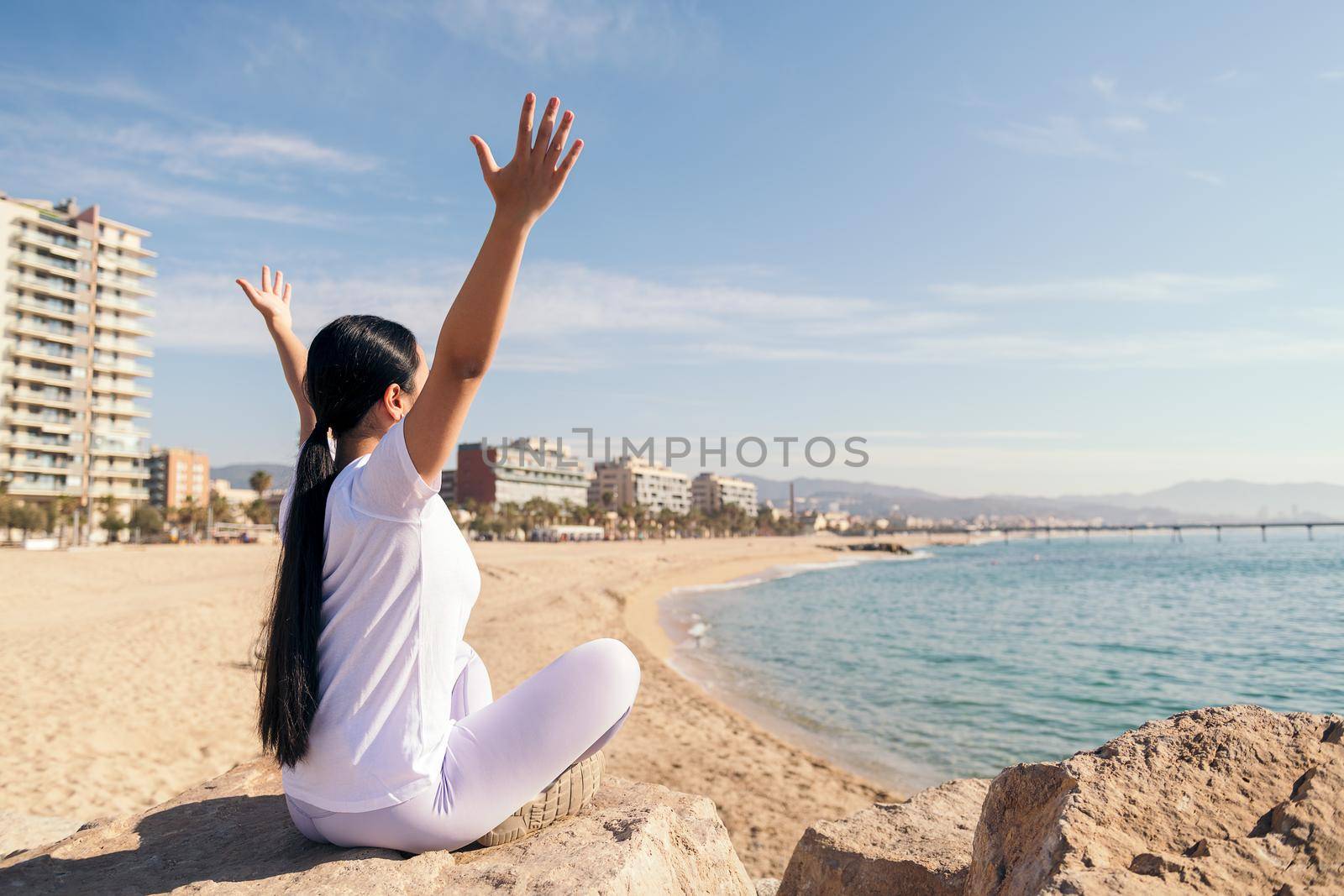 young woman sitting with arms up doing yoga by the beach, concept of spirituality and relax