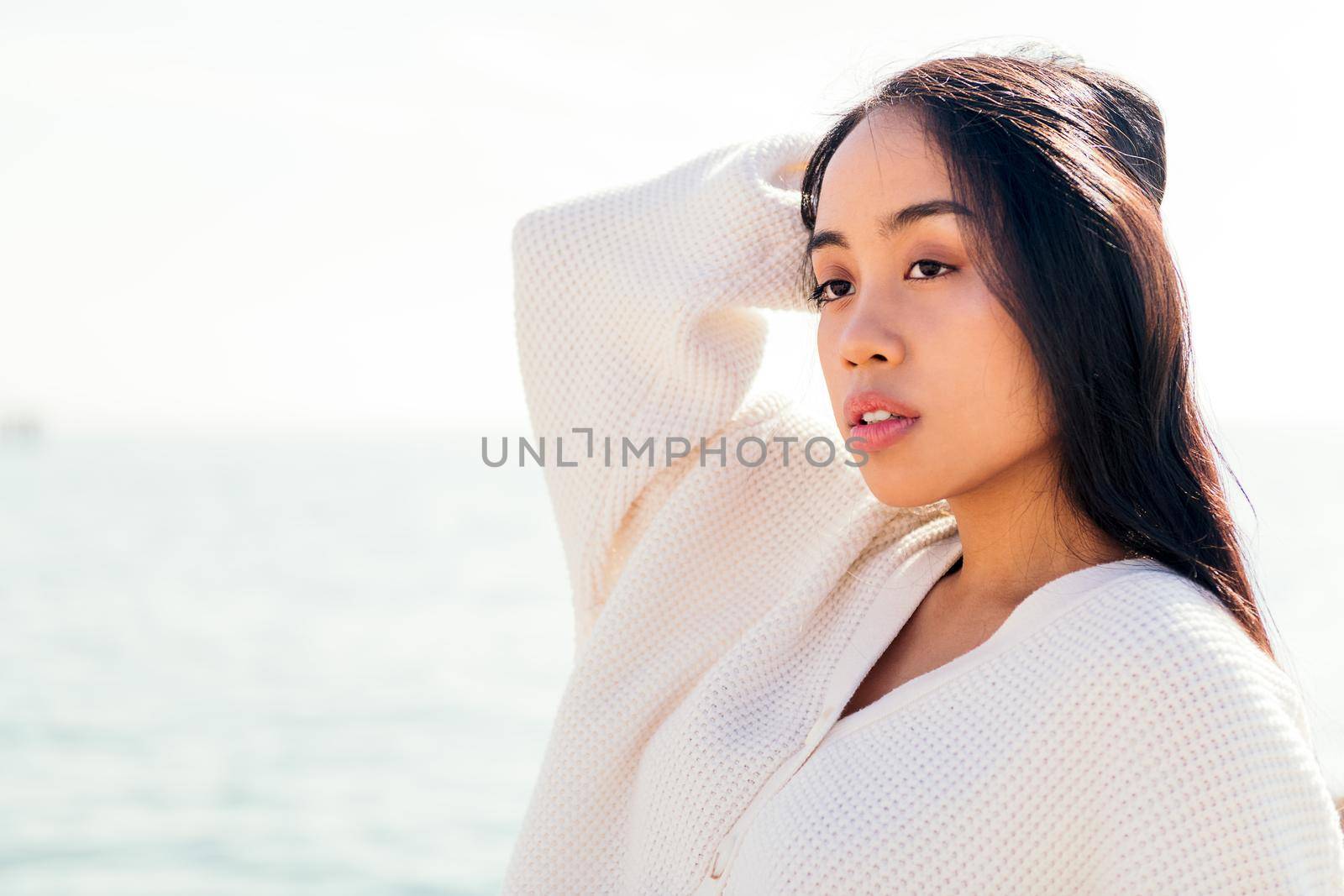 serious young asian woman in white touching her hair, concept of beauty and purity