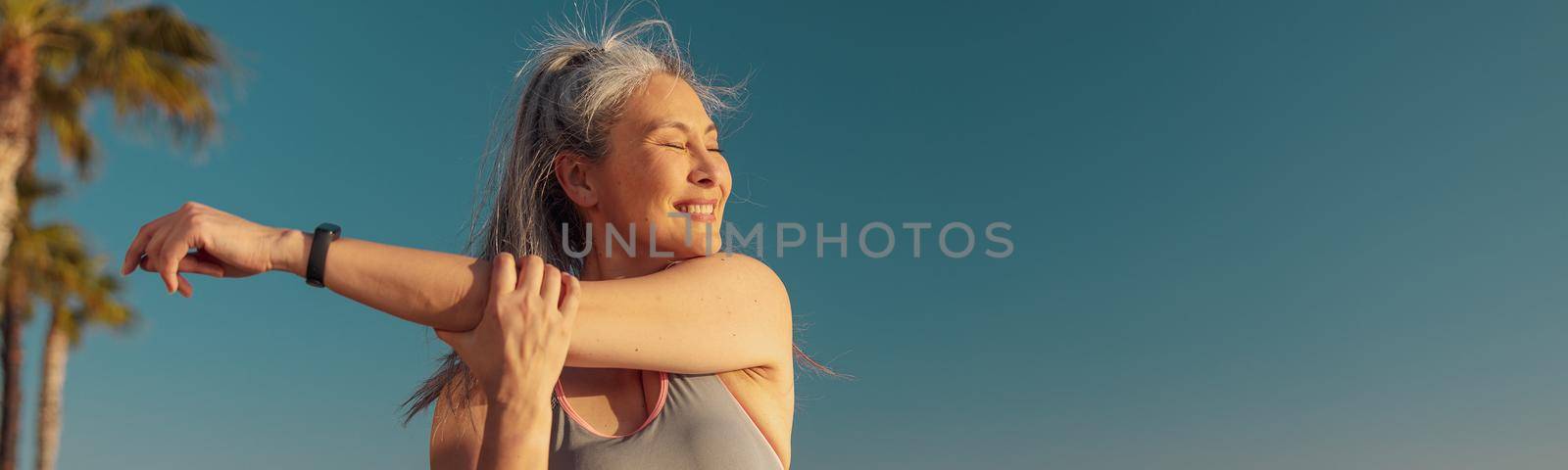 Active female in sportswear doing arm workout on the sports ground on a sunny day by the waterfront