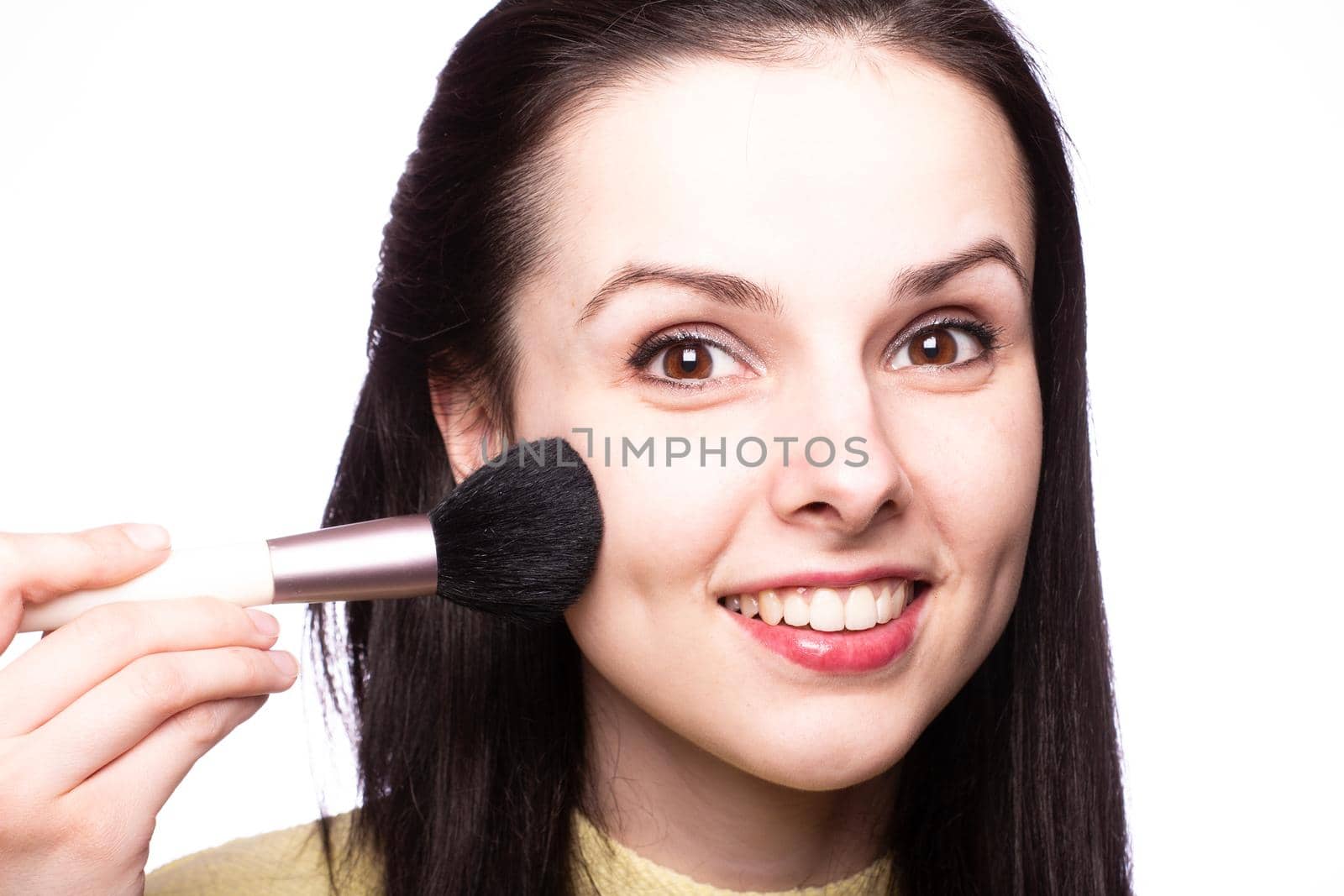 brunette woman in yellow sweater holding makeup brushes. High quality photo