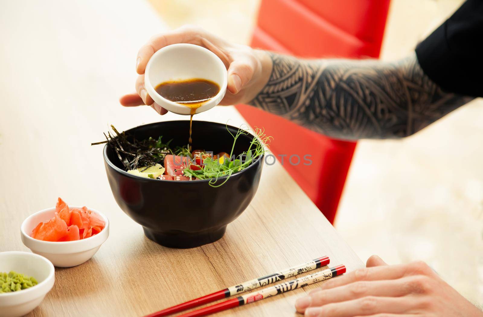 A man adds soy sauce to Poke salad. A man's hand pours soy sauce into a bowl of salad. Guy young man dressing salad with sauce in a restaurant or cafe.