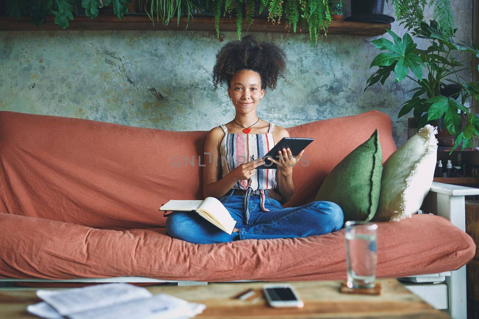 Beautiful African woman scrolling on her tablet and making notes in her living room