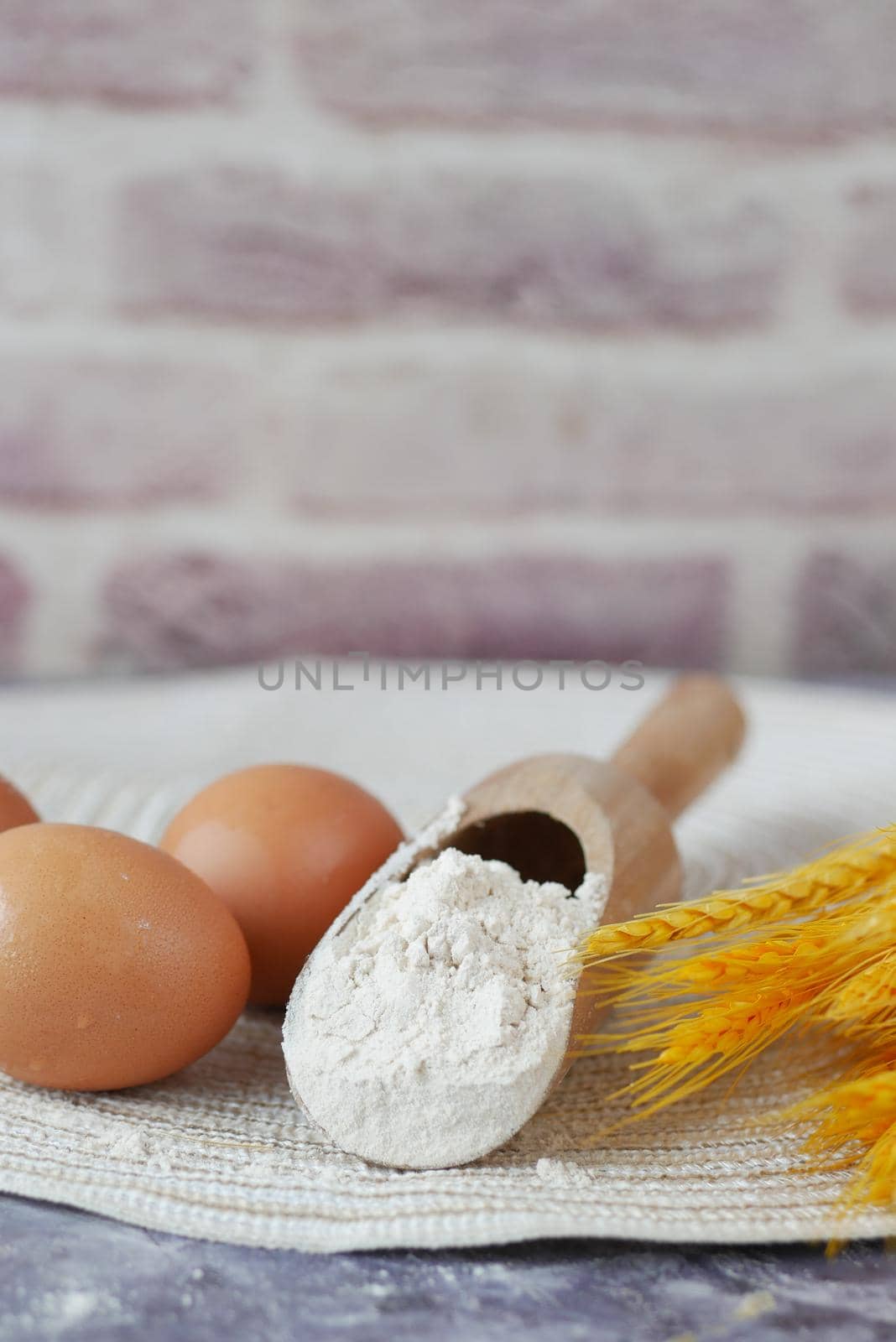 wheat flour in a wooden spoon and eggs on table .