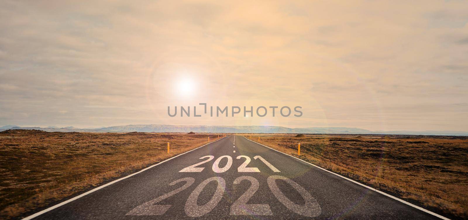 The word 2021 written on highway road in the middle of empty asphalt road at golden sunset and beautiful blue sky. Concept 2021