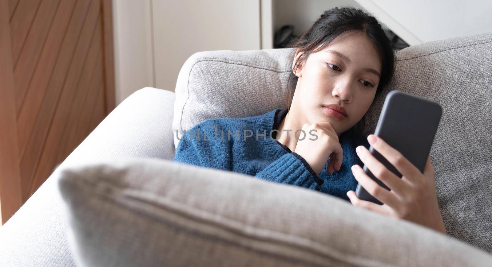 Asian lay on couch in living room frustrated with slow Internet connection or spam on smartphone. by wichayada