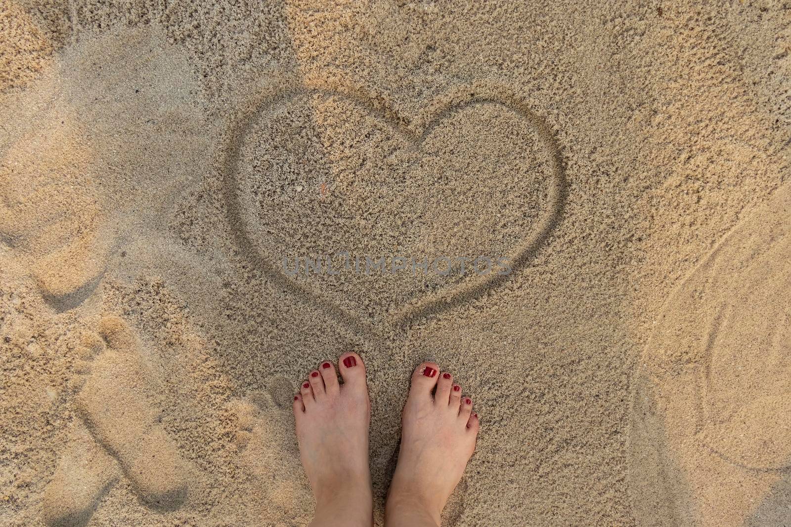 concept of relaxation by the sea on a bright, hot and sunny day on the beach. top view of beautiful female feet with red pedicure on the sea sand by Leoschka