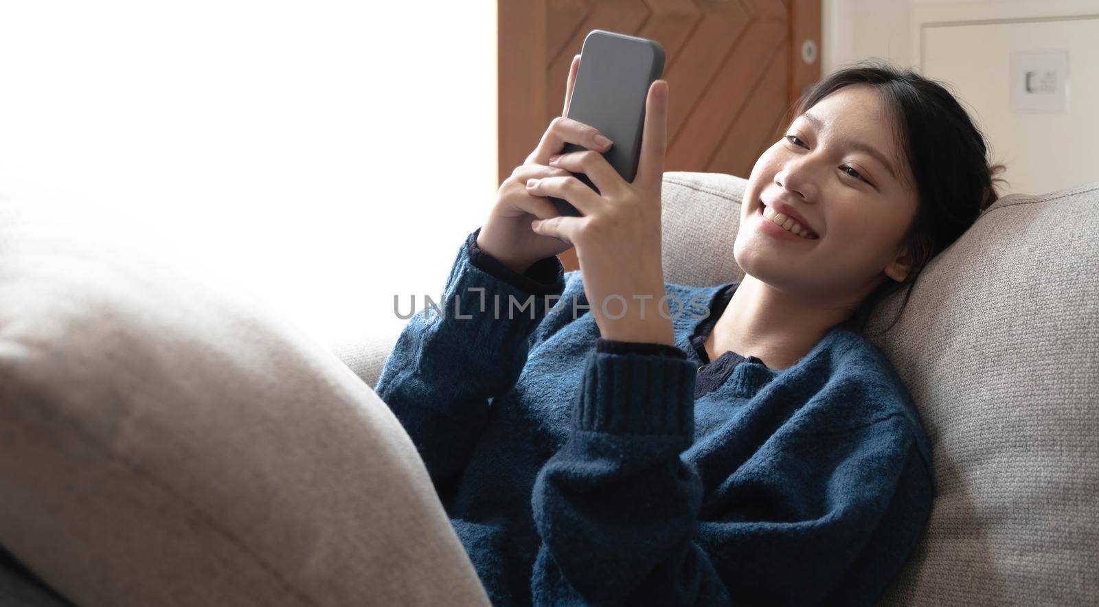 Portrait of smiling happy cheerful beautiful pretty asian woman relaxing making selfie photo on web camera.lying on cozy sofa. by wichayada