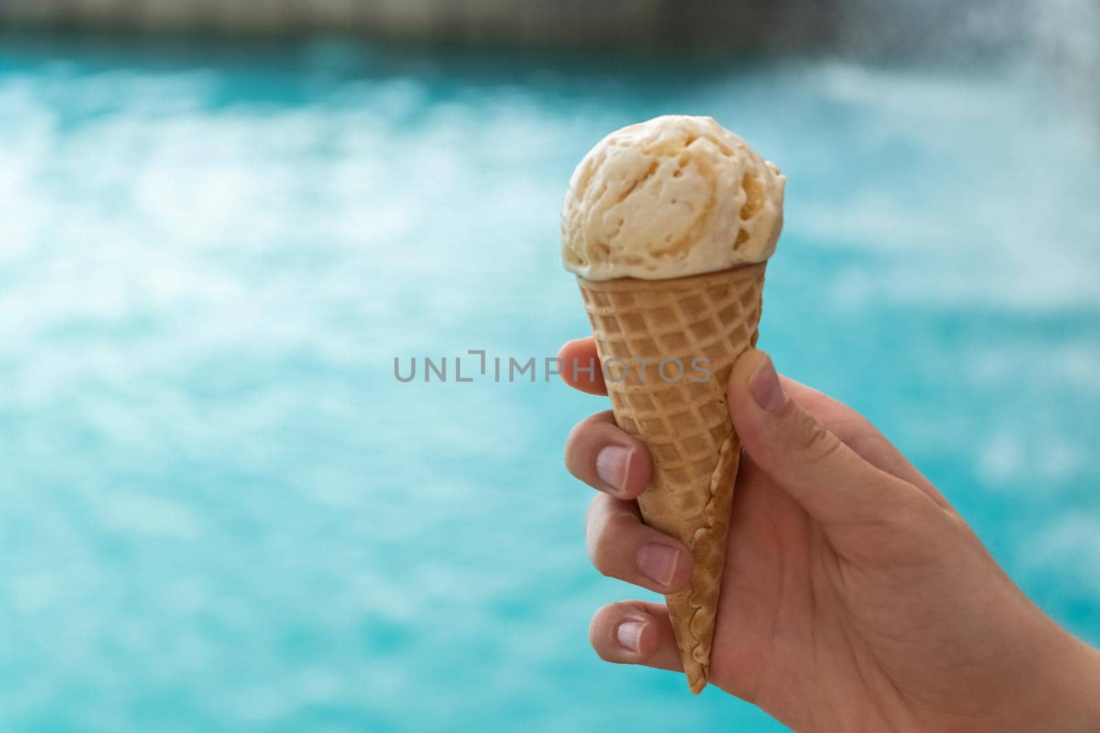 young hand holds an ice cream cone on the background of the blue water of the sea. the concept of relaxation by the sea on a bright, hot and sunny day by Leoschka