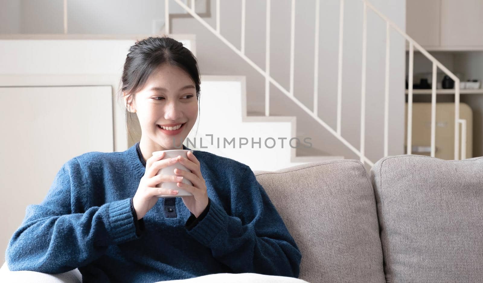 Portrait of smiling happy cheerful beautiful pretty asian woman relaxing drink. Girl felling enjoy having breakfast in holiday morning vacation on sofa at home by wichayada