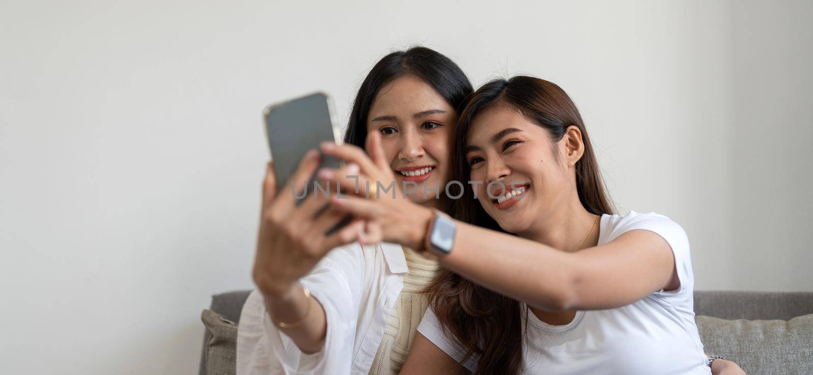 Asian beautiful lesbian or friends using mobile phone to take selfie together on couch. LGBT, Technology and Lifestyle Concept. by nateemee