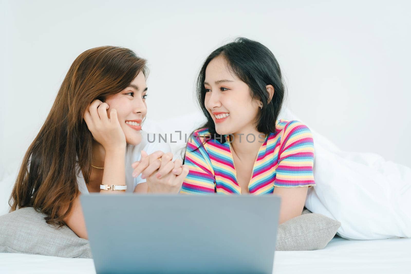 lgbtq, lgbt concept, homosexuality, portrait of two asian women posing happy together and loving each other while playing computer laptop on bed by Manastrong