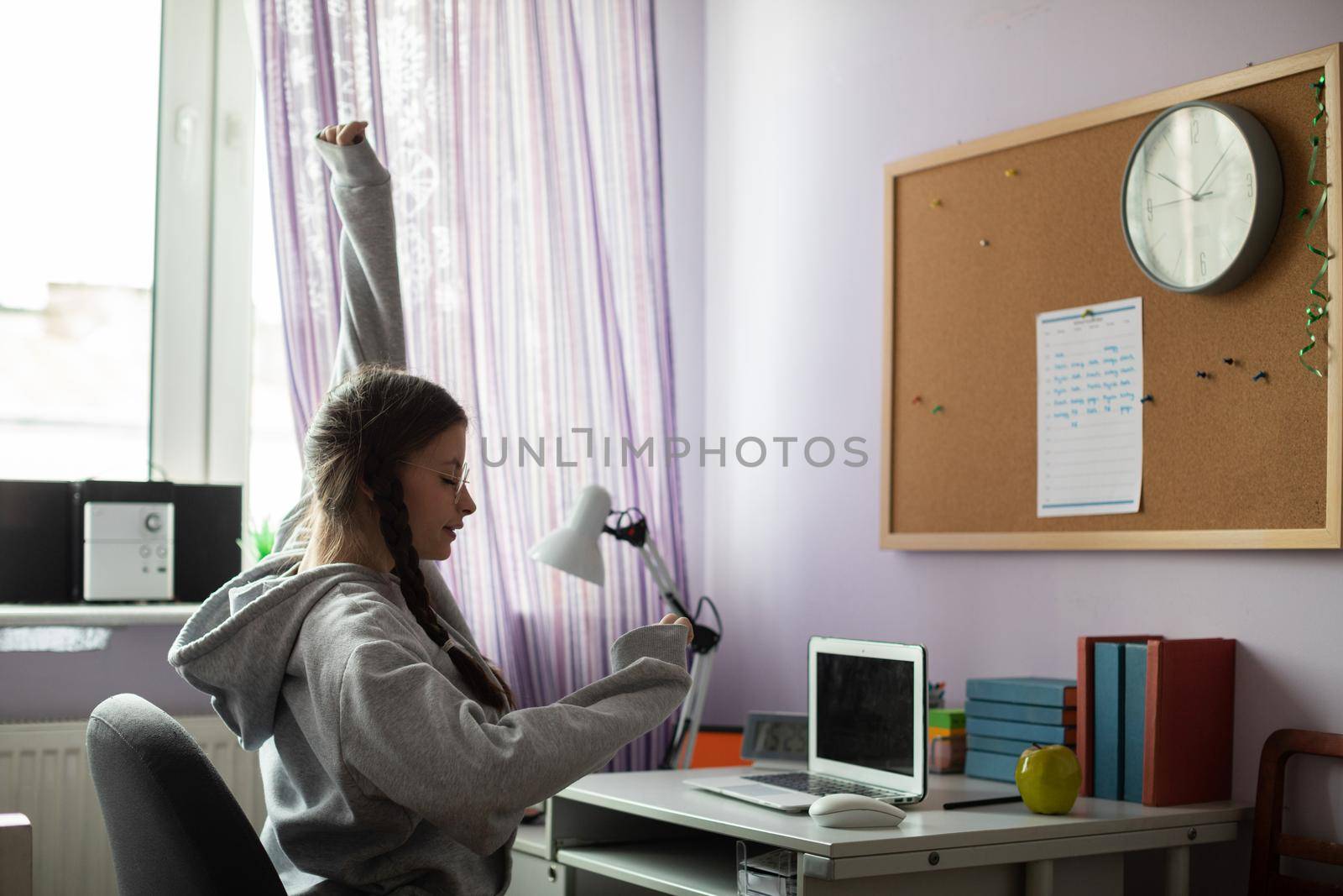 A young girl studies at her desk at home and exercises her hands and arms every now and then. A talented student. Young girl with braids.