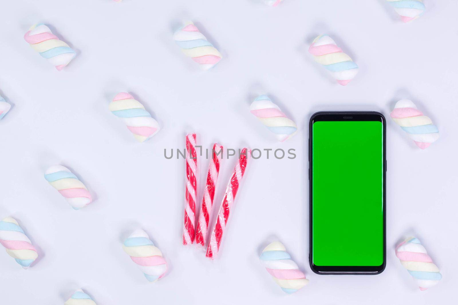 Phone mobile telephone with a vertical green screen. Candy cane Christmas candies. White background with twisted marshmallow pattern. Chroma key smartphone technology. Phone mockup. by JuliaDorian
