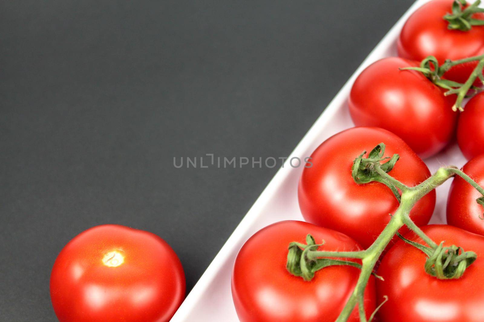 Red tomatoes on white plate on black background