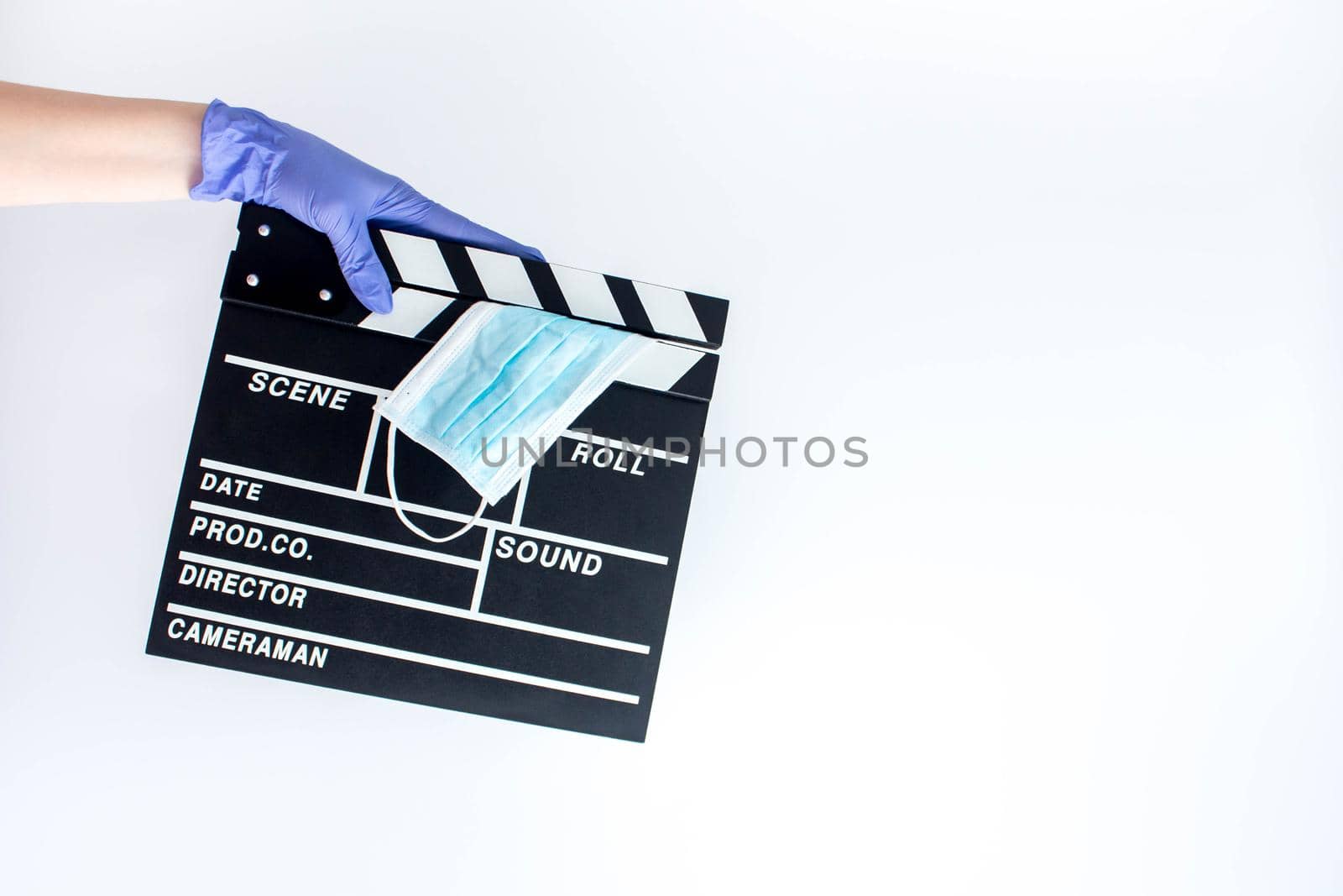 Hand in blue disposable rubber glove holding closed movie clapper with medical mask. Influence of pandemic on cinematography by JuliaDorian