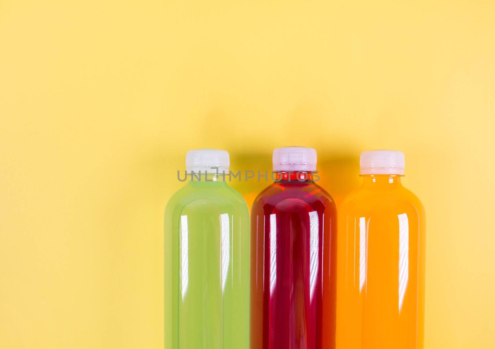 Bottles of orange, green, red smoothie on yellow background. Top view. Flat lay. Copy space. Detox summer drink. Healthy fresh juice bottle. Vegan and vegetarian concept. by JuliaDorian