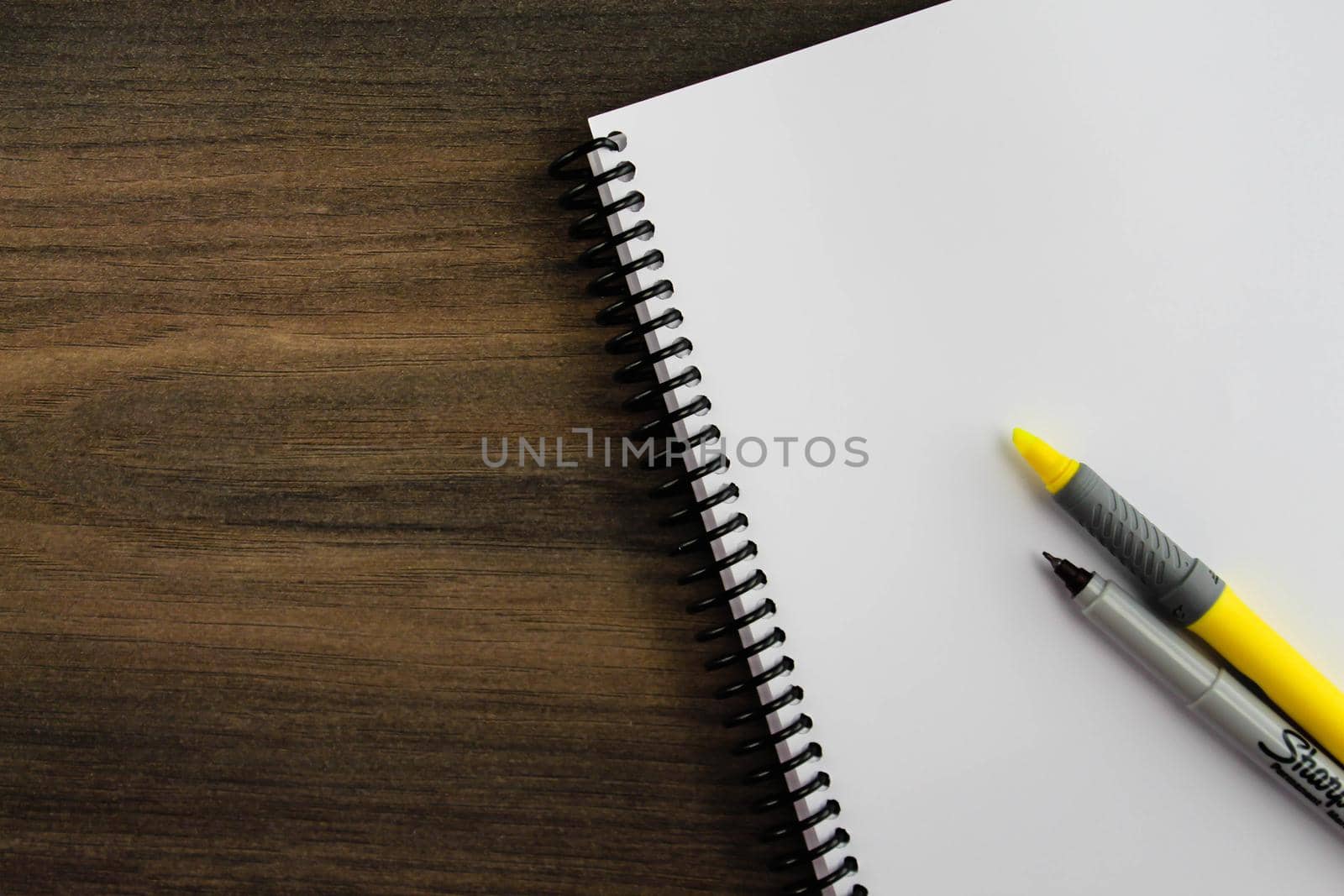 Spiral notepad paper with highlighter and pen on the wooden background. Space for text