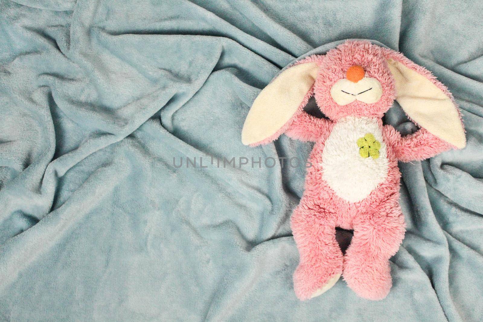 A plush bunny toy sitting on plush blanket and white wall. Plush pink bunny toy with pink knitted octopus.