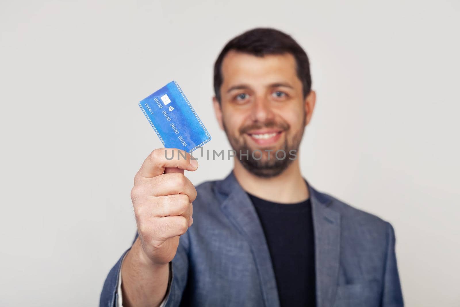 Young businessman man with beard smiling, holding credit card with happy face, standing and smiling with confident smile, showing teeth.