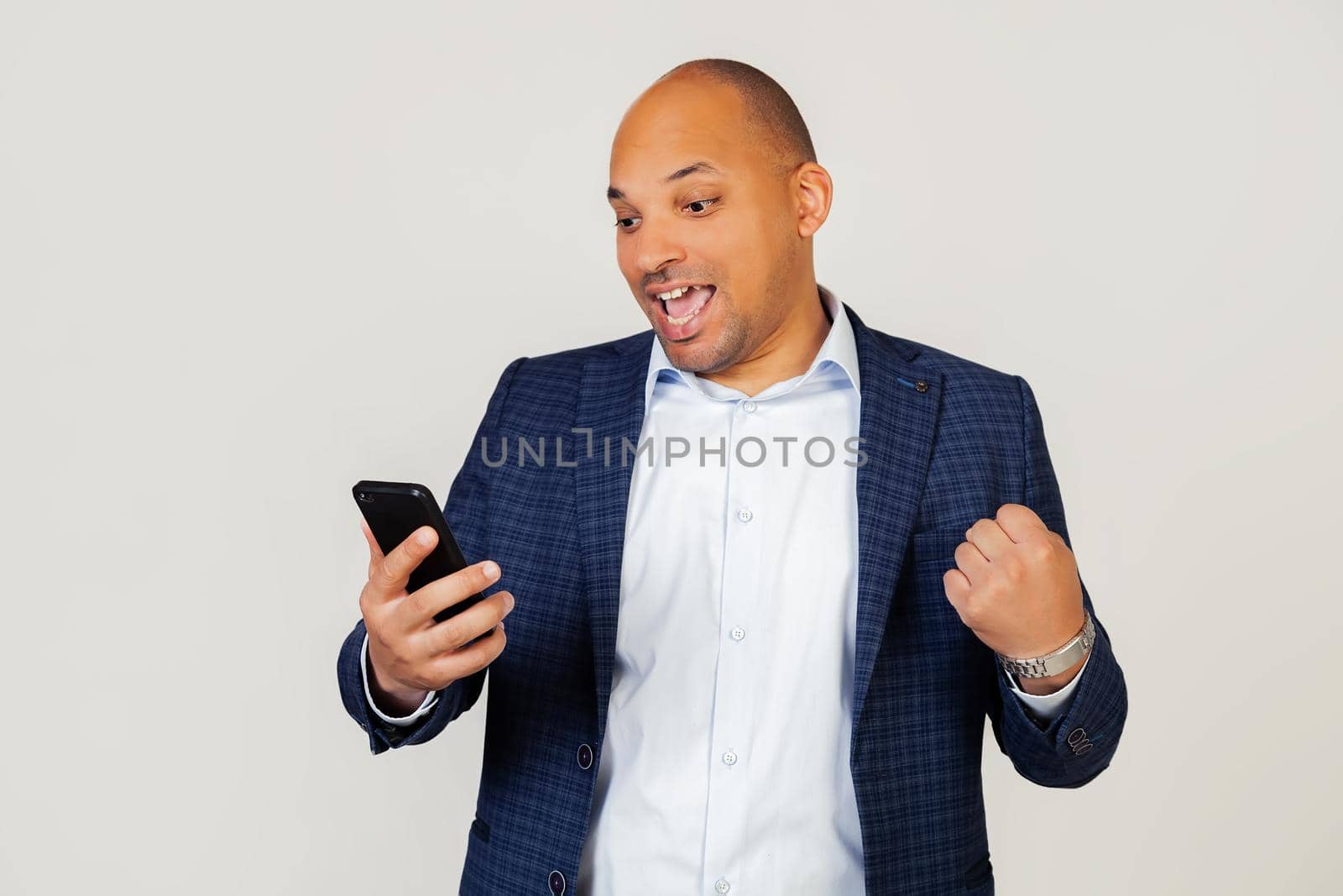 Portrait of happy young african american businessman guy using smart phone, screaming with pride and celebrating victory and success, very excited, rejoicing emotions. Standing on a gray background.