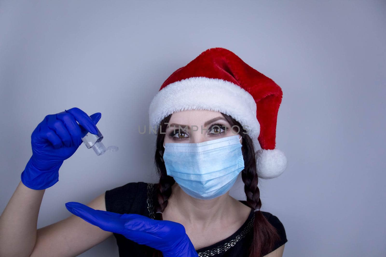 Woman wearing protection face mask against coronavirus. Woman in a mask and Christmas hat with sanitizer. Funny Christmas accessory. Medical mask, Close up shot, Select focus, Prevention from covid19