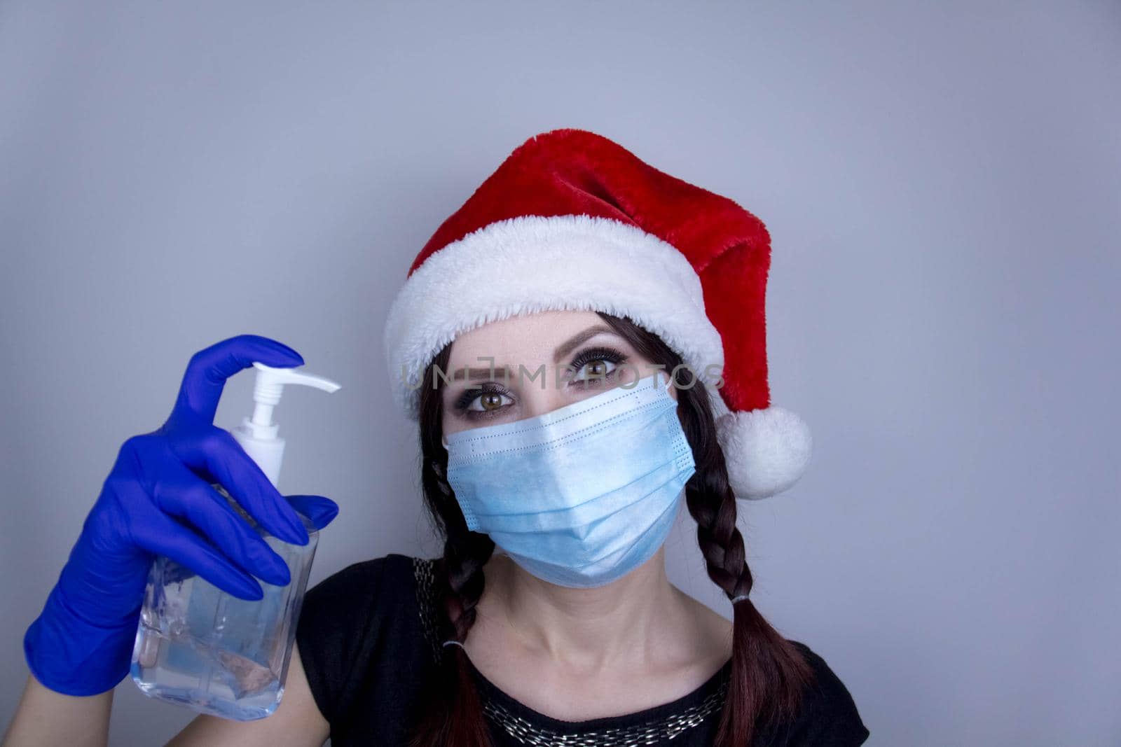 Woman in a mask and Christmas hat with sanitizer. Funny Christmas accessory. Medical mask, Close up shot, Select focus, Prevention from covid19 by JuliaDorian
