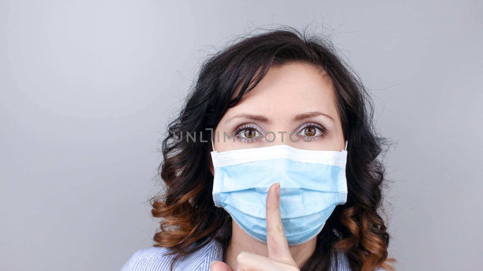 Woman in medical face mask shows finger gesture to be quiet by JuliaDorian