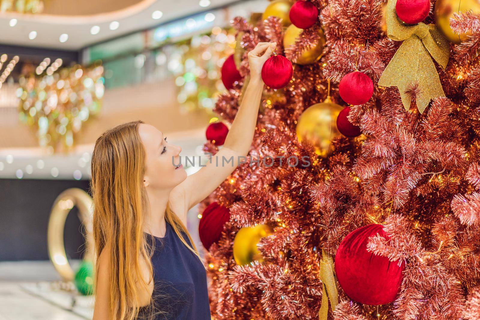 Woman hangs a decoration on the red Christmas tree. Red Christmas tree on the background of lights.