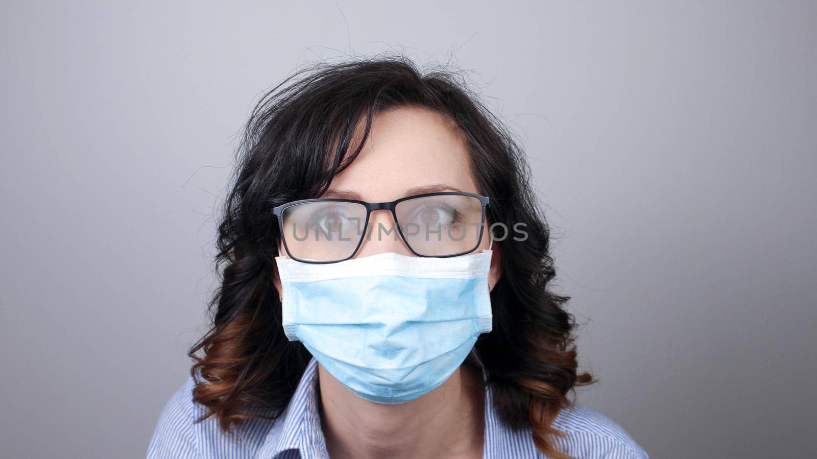 Woman wearing protection face mask against coronavirus and misted glasses. Woman in a mask looking in a mirror. by JuliaDorian