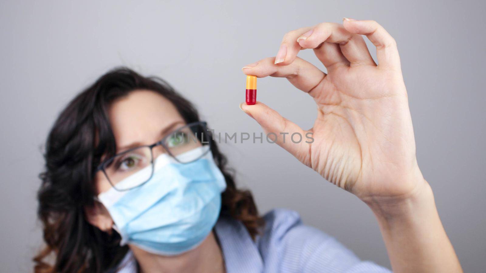 Woman wearing protection face mask against coronavirus and glasses. Woman in a mask showing medicine pill, vaccine. by JuliaDorian