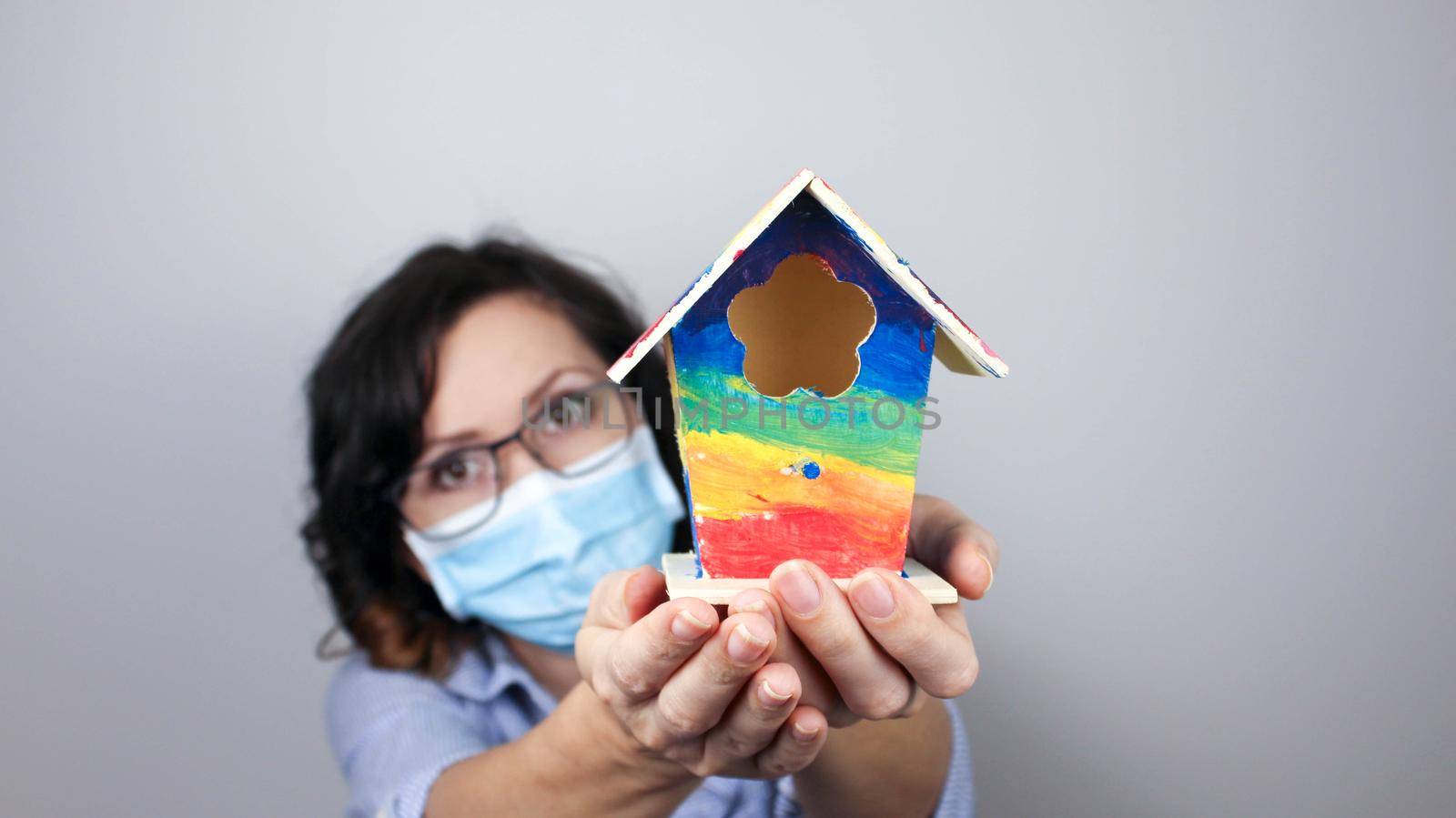Woman wearing protection face mask against coronavirus and glasses. Woman in a mask showing rainbow house. We will be okay. by JuliaDorian