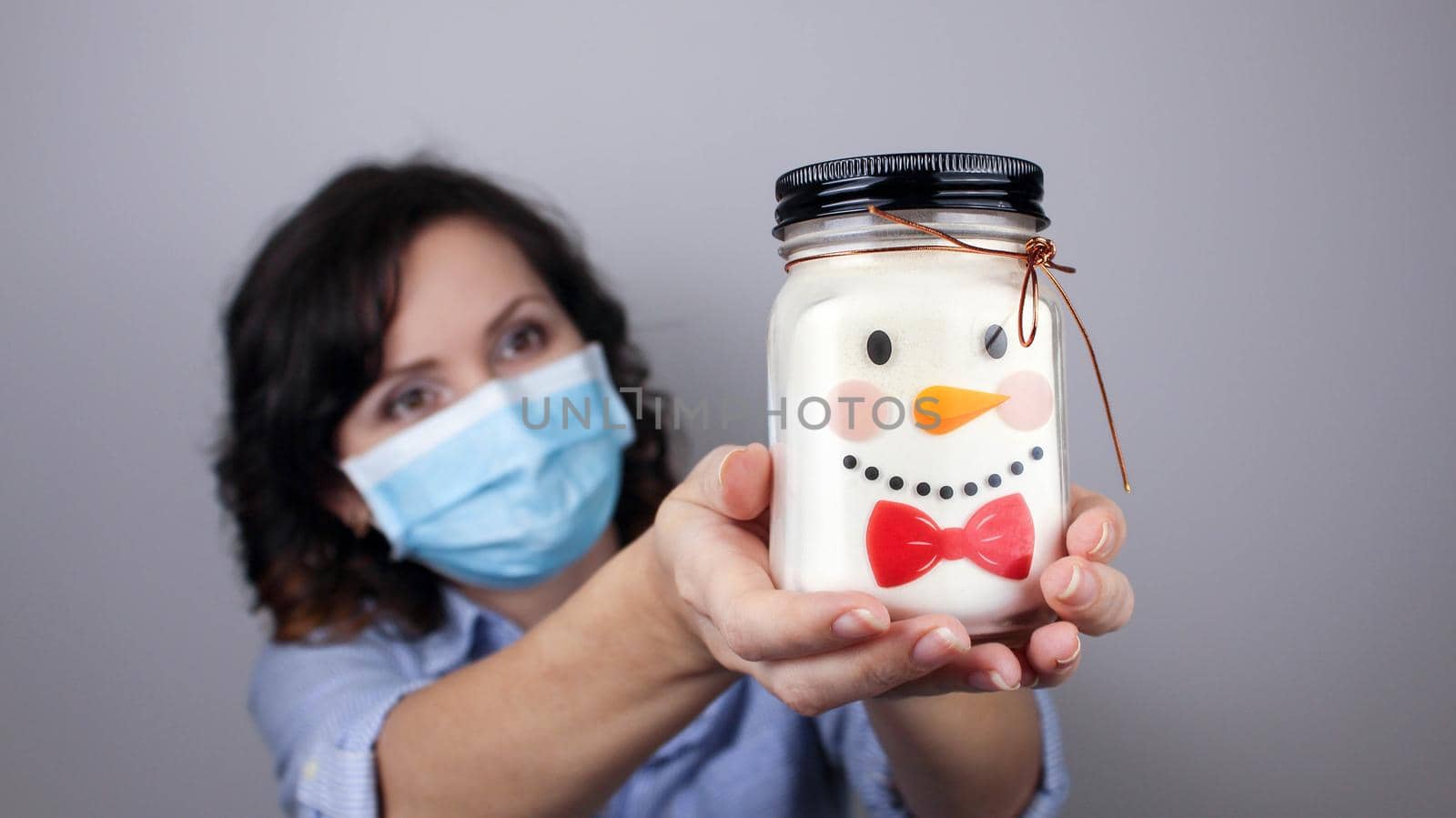 Woman wearing protection face mask against coronavirus. Woman in a mask showing snowman. Can with a Christmas face. We will be okay. Medical mask, Close up shot, Select focus, Prevention from covid19
