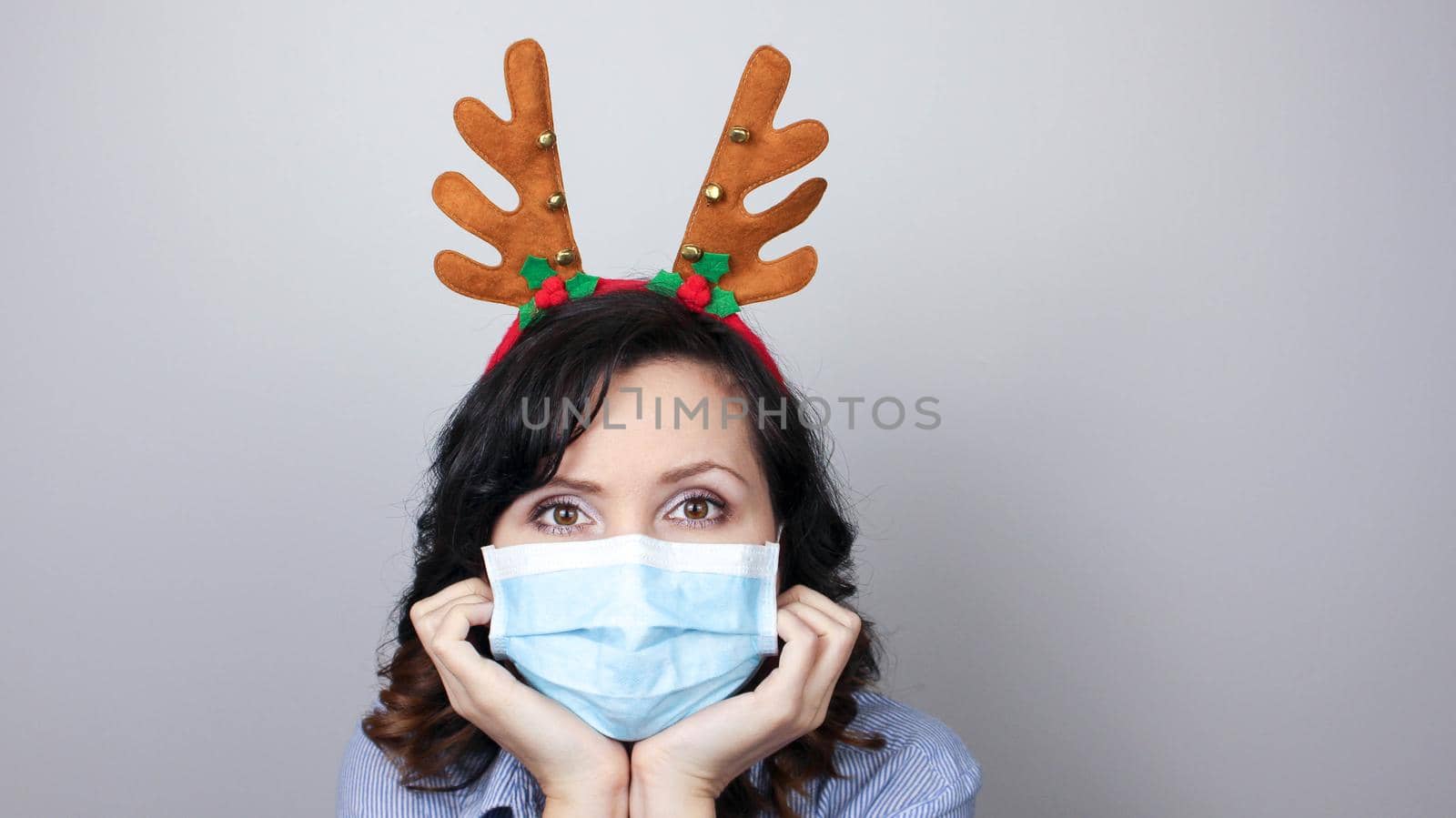 Woman wearing protection face mask against coronavirus. Woman in a mask and deer horns headband. Funny Christmas accessory. Medical mask, Close up shot, Select focus, Prevention from covid19