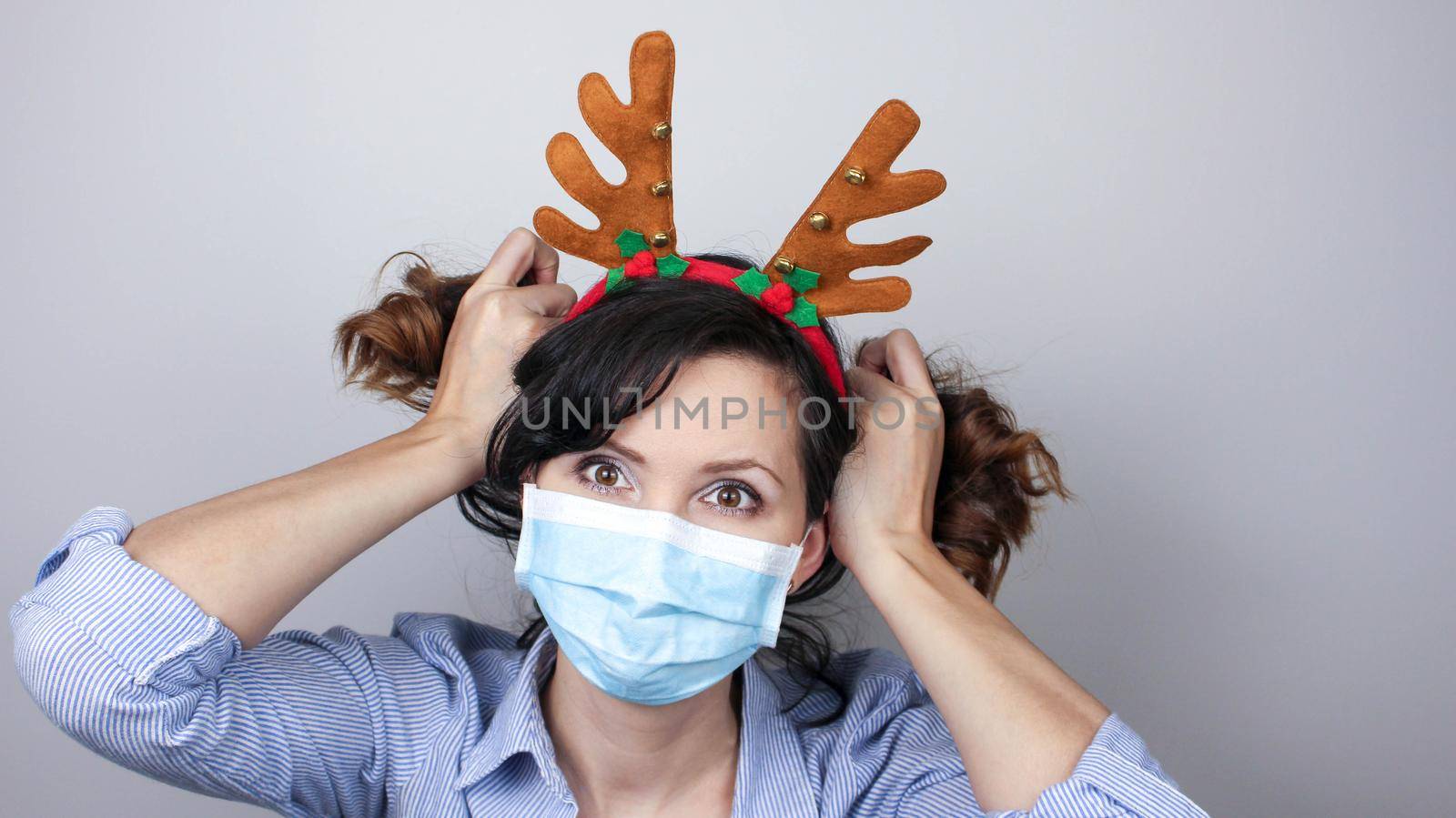 Woman wearing protection face mask against coronavirus. Woman in a mask and deer horns headband. Funny Christmas accessory. Medical mask, Close up shot, Select focus, Prevention from covid19