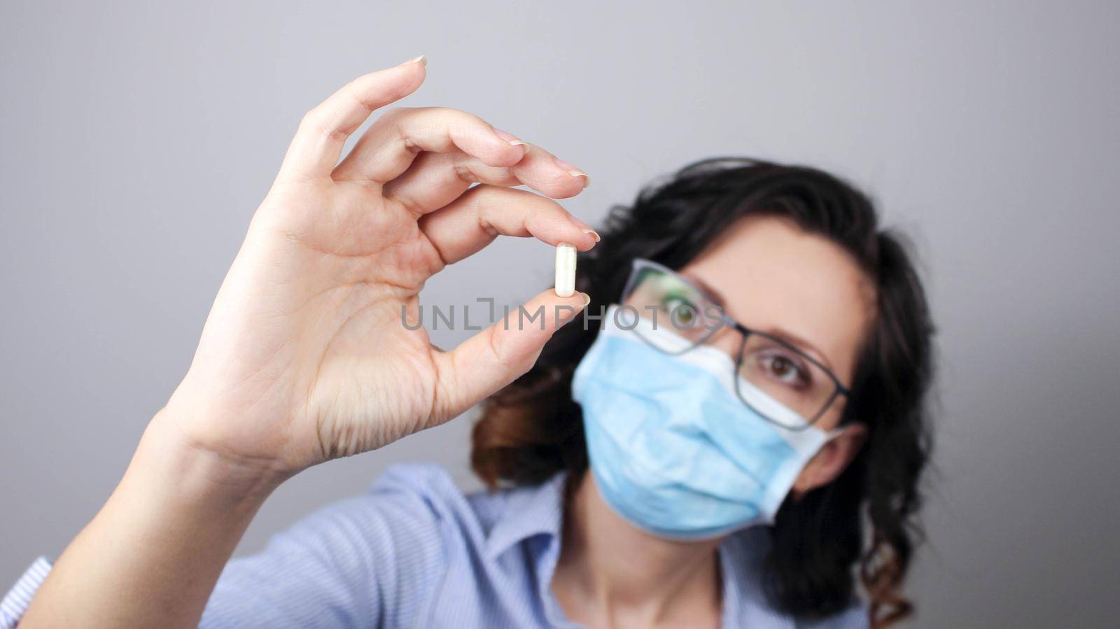 Woman wearing protection face mask against coronavirus and glasses. Woman in a mask showing medicine pill, vaccine. Medical mask, Close up shot, Select focus, Prevention from covid19