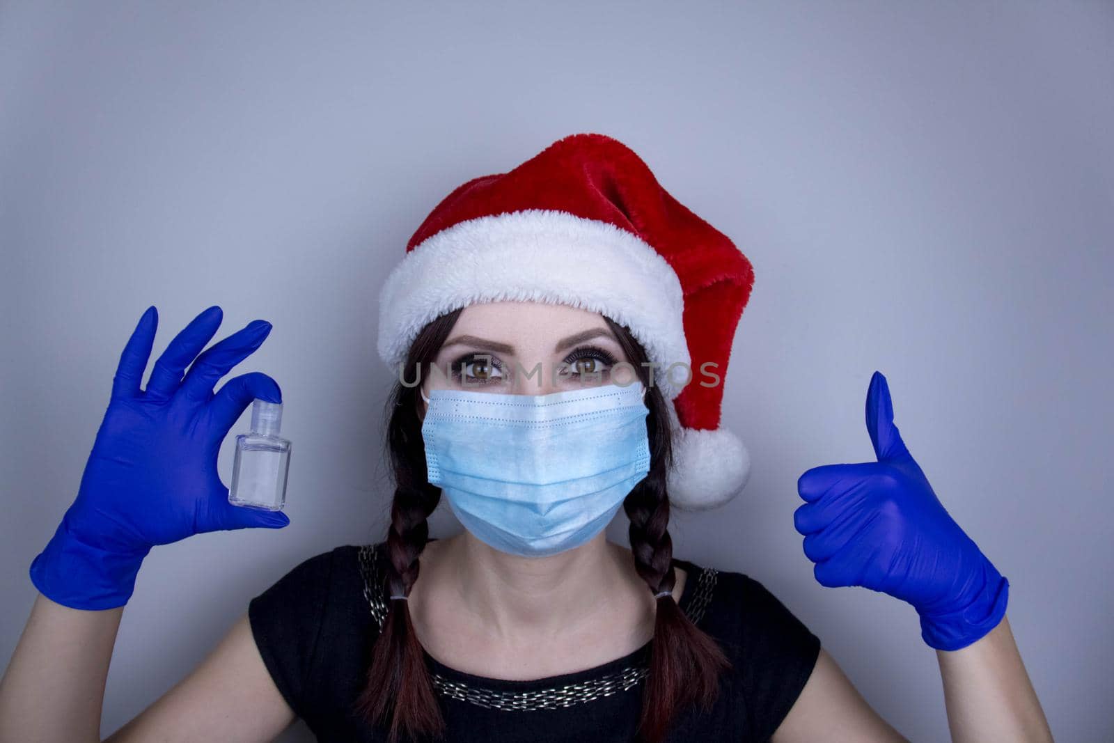 Woman in a mask and Christmas hat with sanitizer. Funny Christmas accessory. Medical mask, Close up shot, Select focus, Prevention from covid19 by JuliaDorian