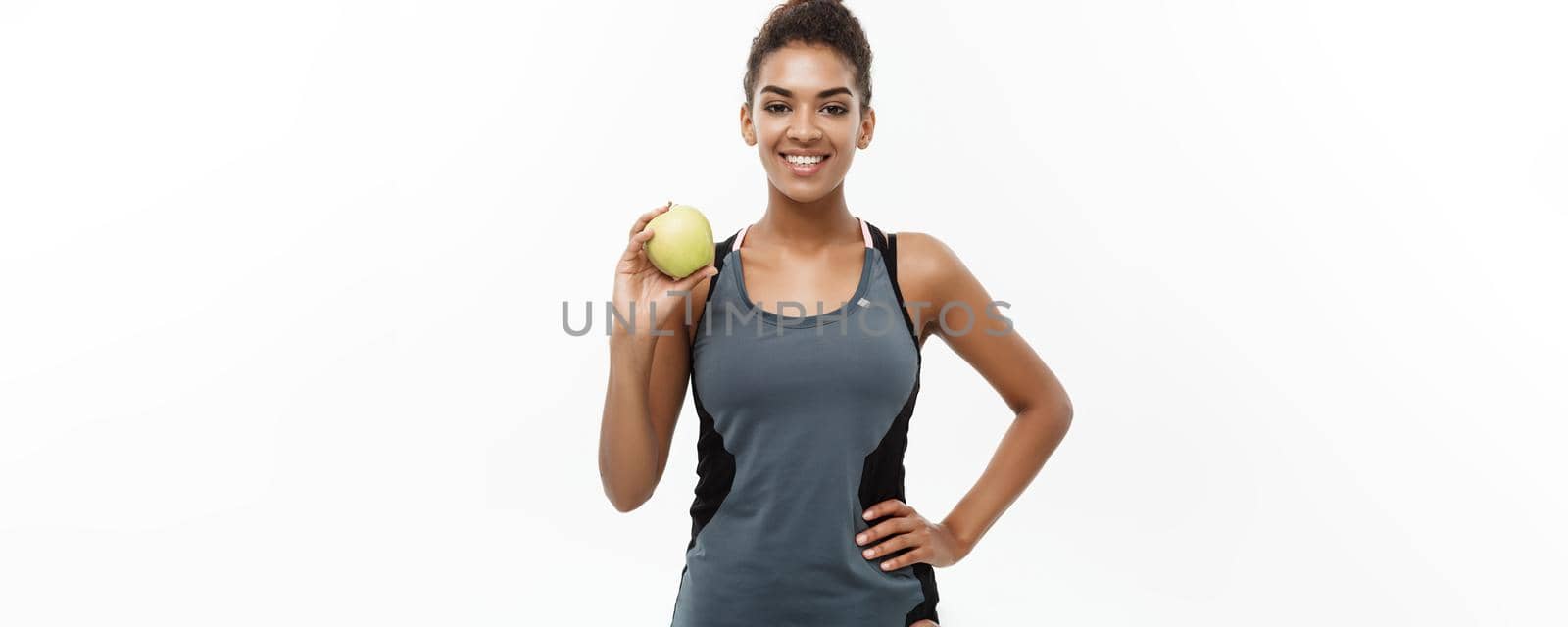 Healthy and Fitness concept - Beautiful American African lady in grey fitness clothes holding green apple. Isolated on white background