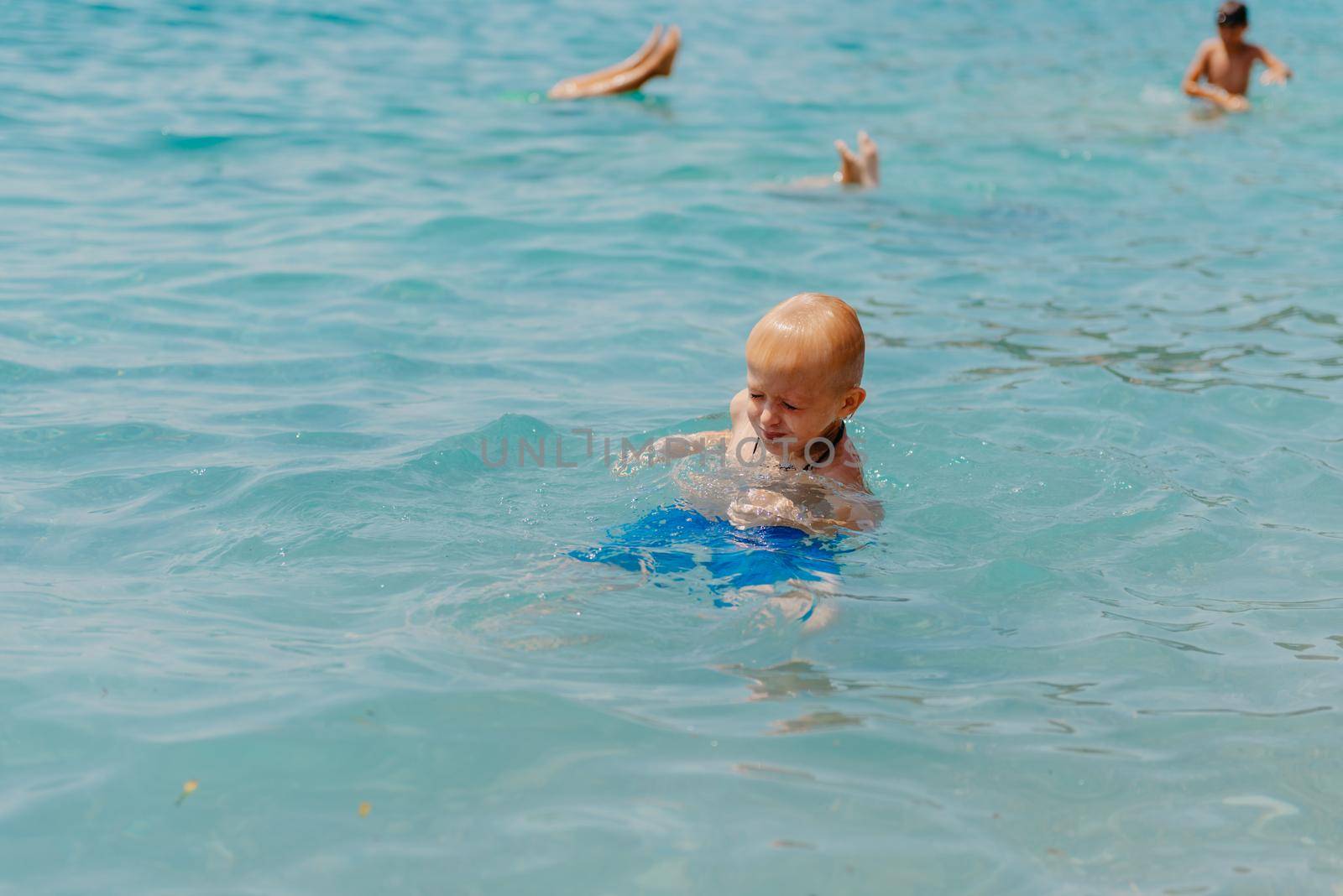 Child learning to swim in the open sea of tropical resort. Kids learn swimming. Exercise and training for young children. Little boy with colorful float board in sport club. Swimming baby or toddler. Happy child boy swims in sea in swimming circle with splash. Blue sky and water. Swimming training. Fun joy activities on vacation in the beach. Childhood moments lifestyle. Freedom careless. boy swim in the sea by Andrii_Ko