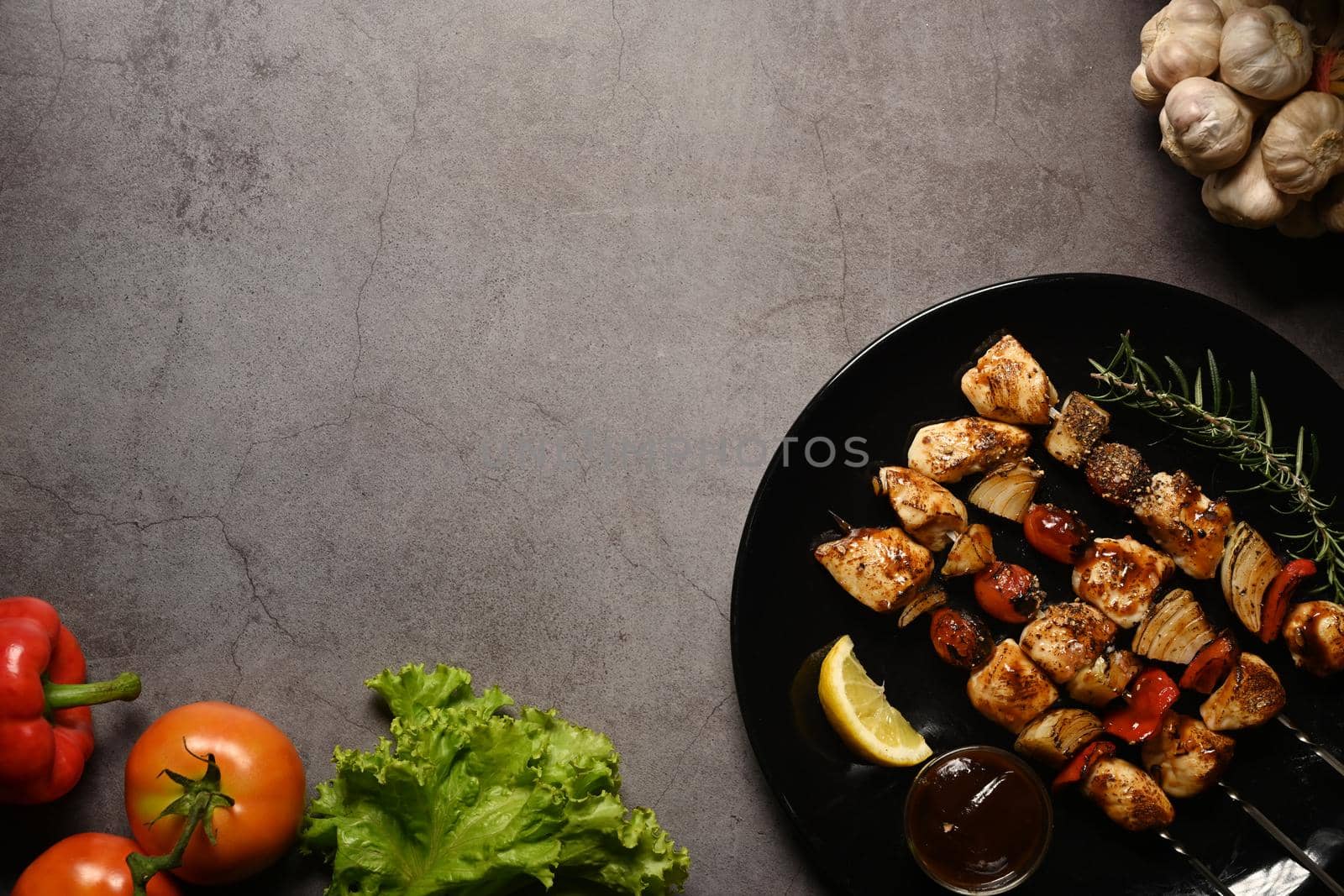 Grilled chicken meat skewers with fresh vegetables on dark stone background. Copy space for your text.